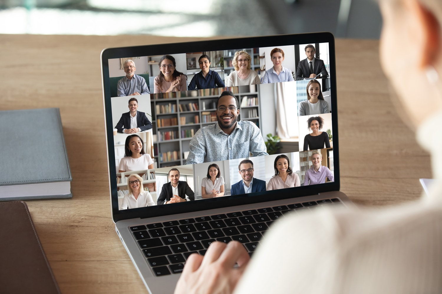 Someone attends a virtual meeting on their laptop at home, the smiling faces of many office colleagues on the screen