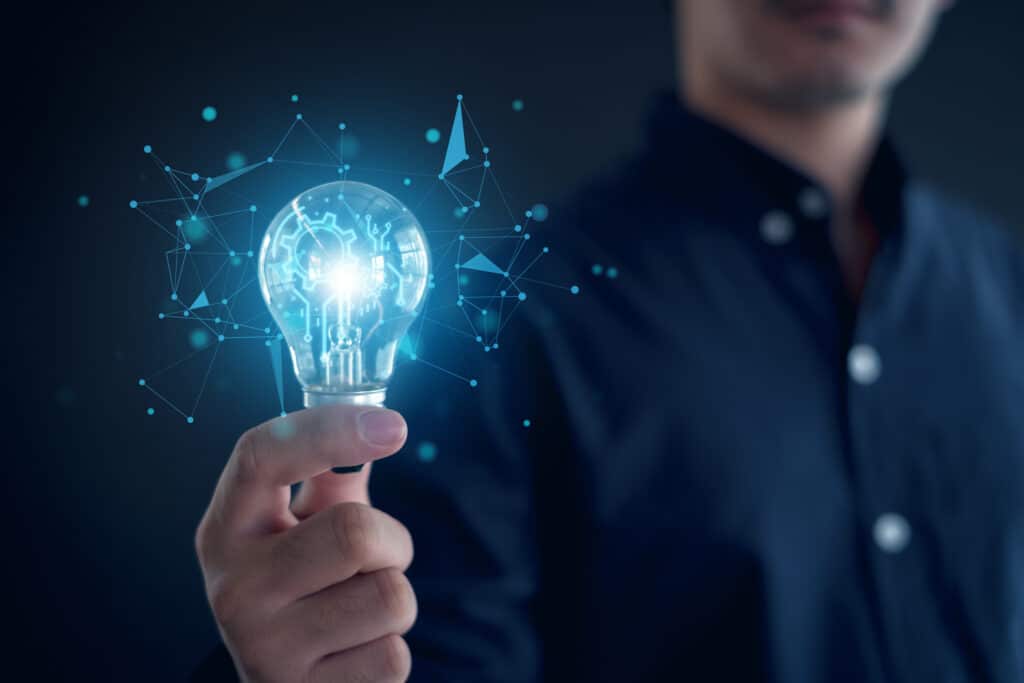 A man holds a glowing lightbulb. A matrix of ideas spill from the bulb as a metaphor for ideas and thoughts.