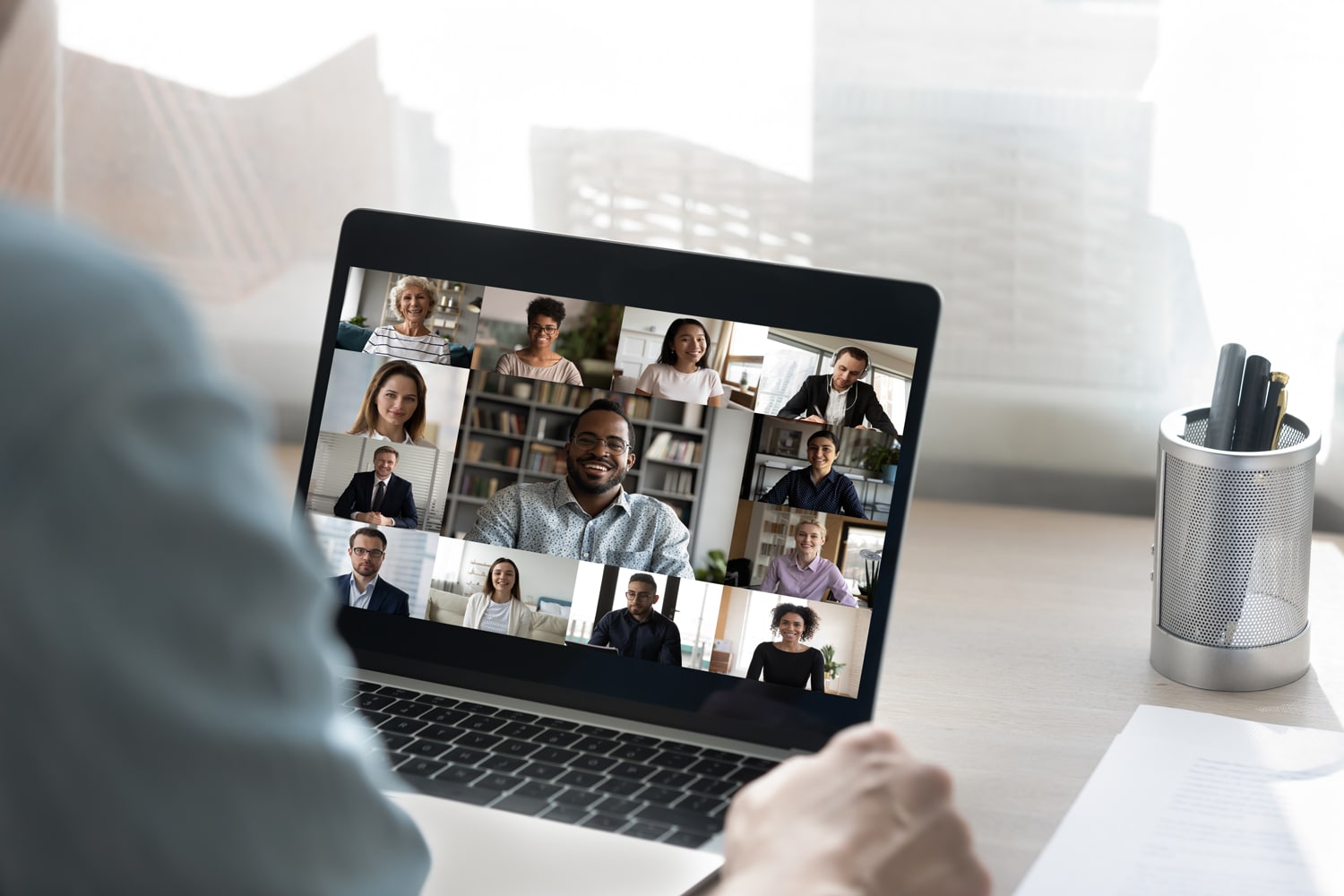 A person attends a virtual event on their laptop. The screen is filled with the faces of professional business people.
